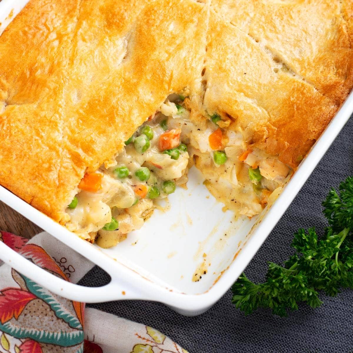 overhead flat lay of chicken pot pie casserole ingredients including raw chicken, diced vegetables, biscuit dough, fresh herbs, and broth on a wooden surface