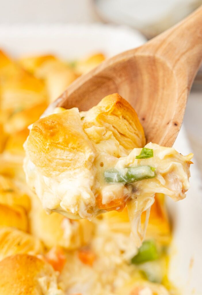 close-up of a spoonful of chicken pot pie casserole being lifted from the dish, showing creamy filling with vegetables and fluffy biscuit topping