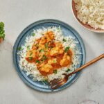 Chicken Tikka Masala served in a white bowl over fluffy basmati rice, garnished with fresh cilantro and a swirl of cream, photographed from above on a warm wooden table