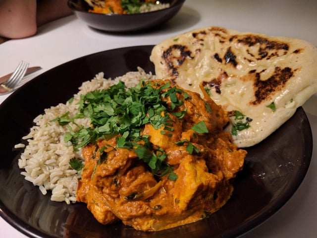 Chicken Tikka Masala — Rich, Aromatic, and Deeply Satisfying 28 Close-up of Chicken Tikka Masala sauce coating tender pieces of charred chicken, with fresh cilantro leaves and a slice of warm naan on the side, shallow depth of field