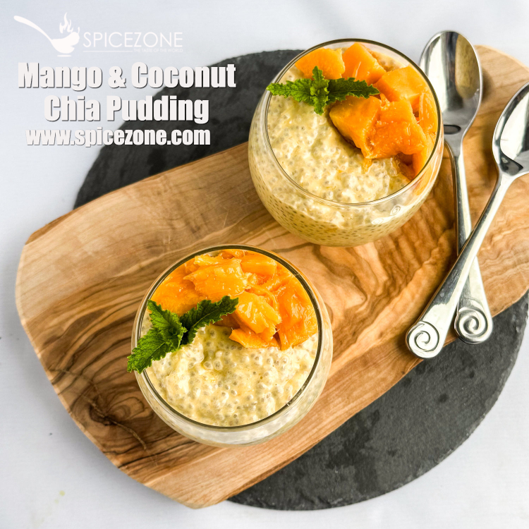 Overhead flat lay of coconut chia pudding ingredients including canned coconut milk, a bowl of chia seeds, fresh mango chunks, pineapple slices, toasted coconut flakes, maple syrup, and vanilla extract arranged on a light wood surface
