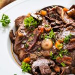 Coq au Vin served in a wide shallow bowl with tender chicken thighs, mushrooms, pearl onions, and glossy red wine sauce, garnished with fresh thyme