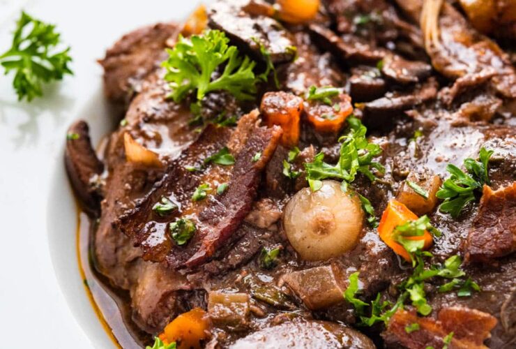 Coq au Vin served in a wide shallow bowl with tender chicken thighs, mushrooms, pearl onions, and glossy red wine sauce, garnished with fresh thyme