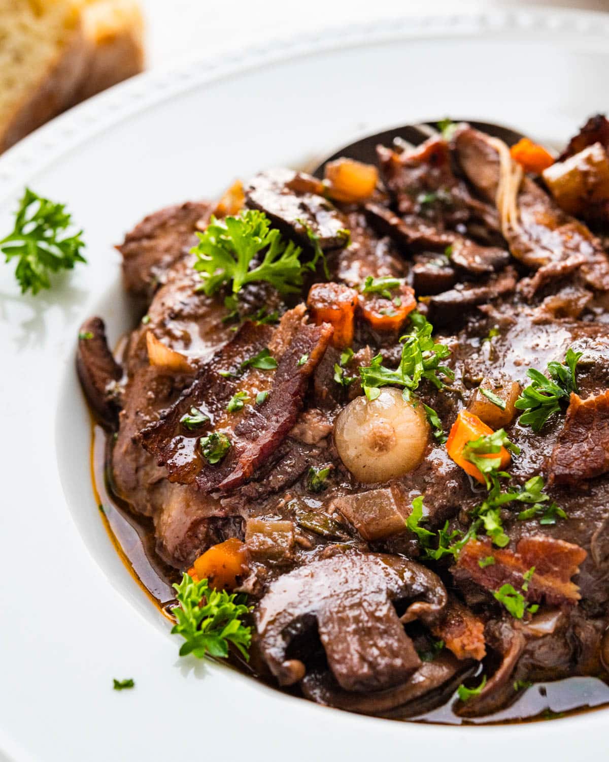 Coq au Vin served in a wide shallow bowl with tender chicken thighs, mushrooms, pearl onions, and glossy red wine sauce, garnished with fresh thyme