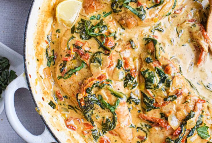 Creamy Tuscan Chicken served in a white skillet with golden pan-seared chicken breasts nestled in a rich spinach and sun-dried tomato cream sauce, garnished with fresh basil