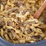 Crockpot beef and noodles served in a wide bowl with tender shredded beef over egg noodles smothered in rich brown gravy, garnished with fresh parsley