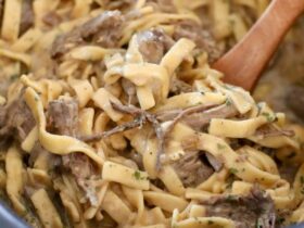 Crockpot beef and noodles served in a wide bowl with tender shredded beef over egg noodles smothered in rich brown gravy, garnished with fresh parsley