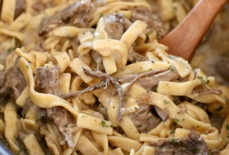 Crockpot beef and noodles served in a wide bowl with tender shredded beef over egg noodles smothered in rich brown gravy, garnished with fresh parsley