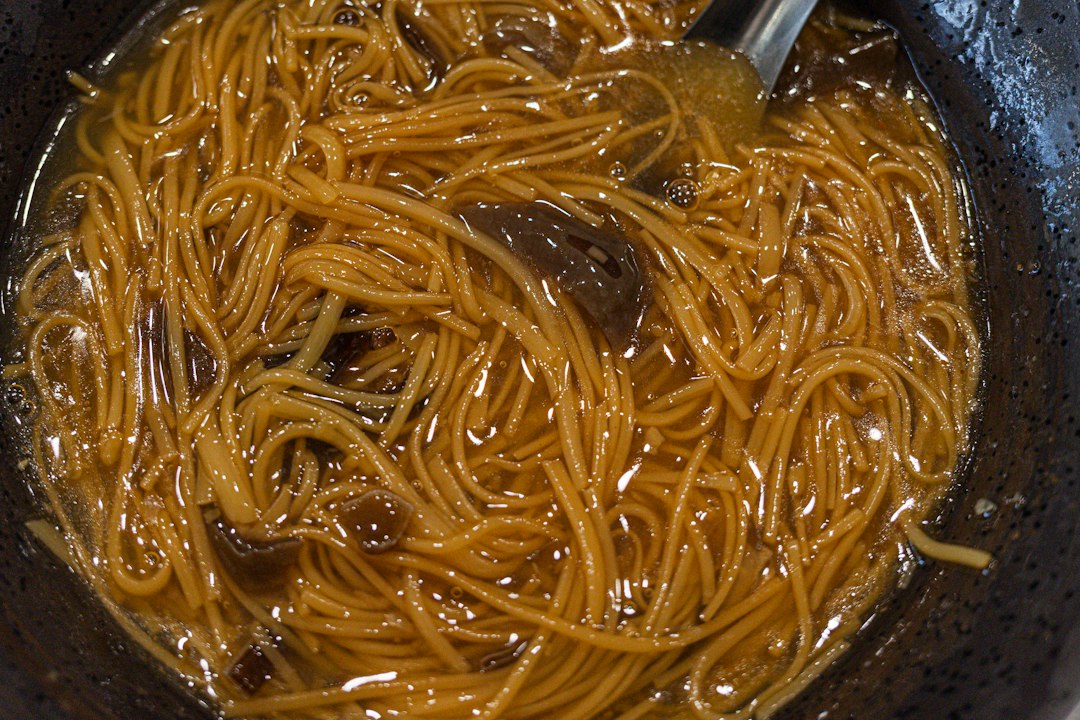 Close-up of a fork lifting tender shredded beef from a bowl of crockpot beef and noodles, showing the glossy brown gravy coating every strand of egg noodle