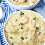 Overhead shot of crockpot chicken and dumplings in a rustic white bowl, fluffy dumplings floating in golden broth with fresh parsley garnish