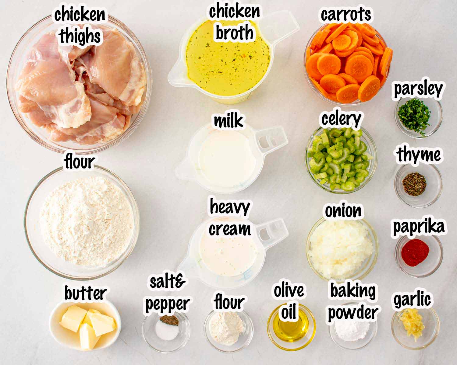 Flat lay of raw ingredients for crockpot chicken and dumplings — chicken thighs, carrots, celery, onion, garlic, flour, fresh herbs, and broth on a wooden surface