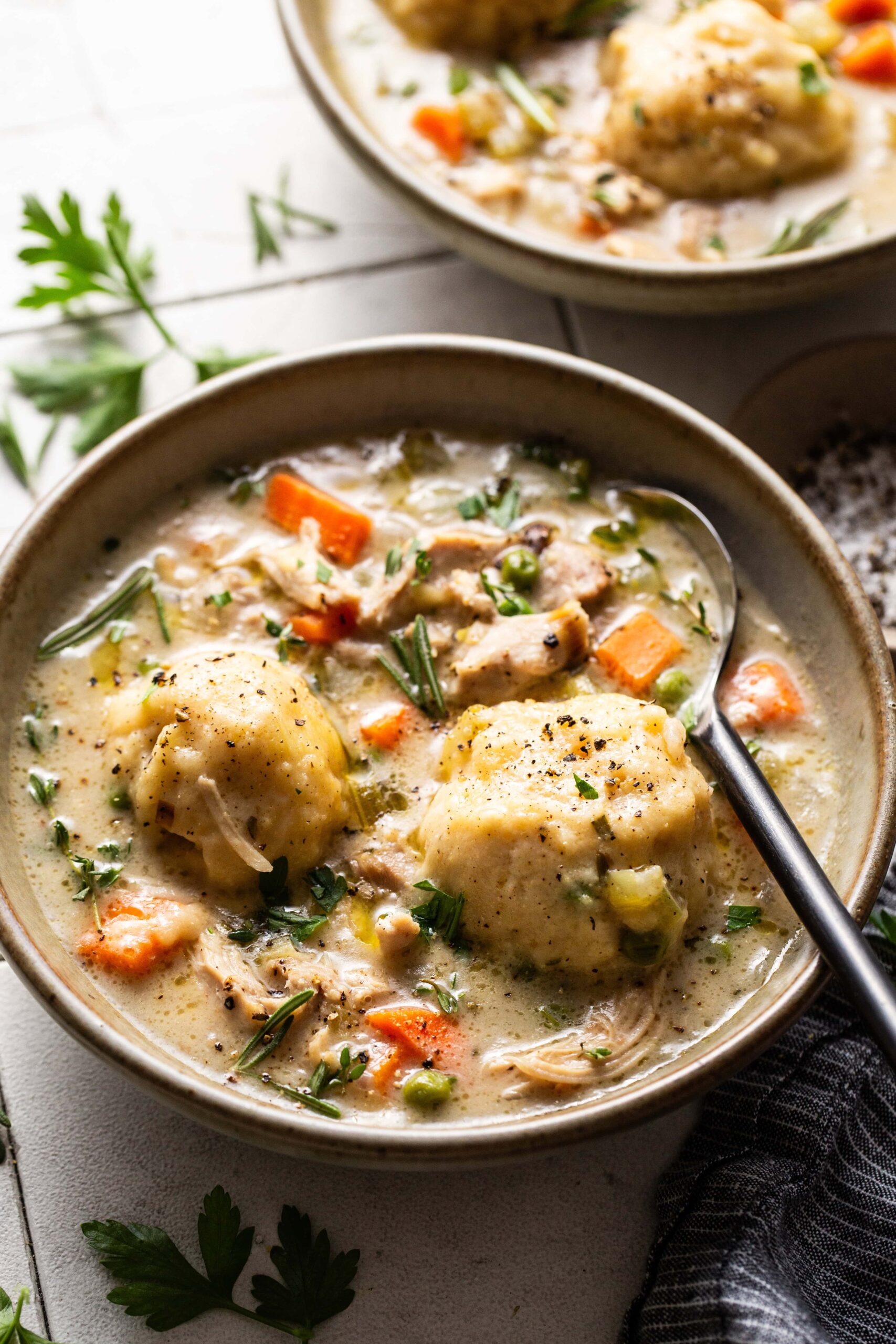 Close-up of a spoonful of crockpot chicken and dumplings being lifted from a bowl, showing fluffy dumpling texture and shredded chicken in golden broth