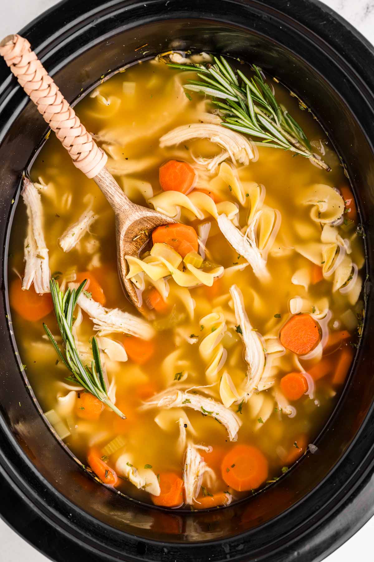 Crockpot Chicken Noodle Soup — The Ultimate From-Scratch Slow Cooker Comfort Bowl 26 A steaming bowl of Crockpot Chicken Noodle Soup with golden broth, tender shredded chicken, thick egg noodles, and sliced carrots, garnished with fresh parsley, photographed overhead on a rustic wooden table