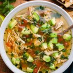 Crockpot Chicken Tortilla Soup served in a rustic bowl topped with tortilla strips, avocado, shredded cheese, cilantro, and a lime wedge on a warm wooden table