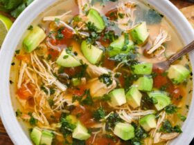 Crockpot Chicken Tortilla Soup served in a rustic bowl topped with tortilla strips, avocado, shredded cheese, cilantro, and a lime wedge on a warm wooden table