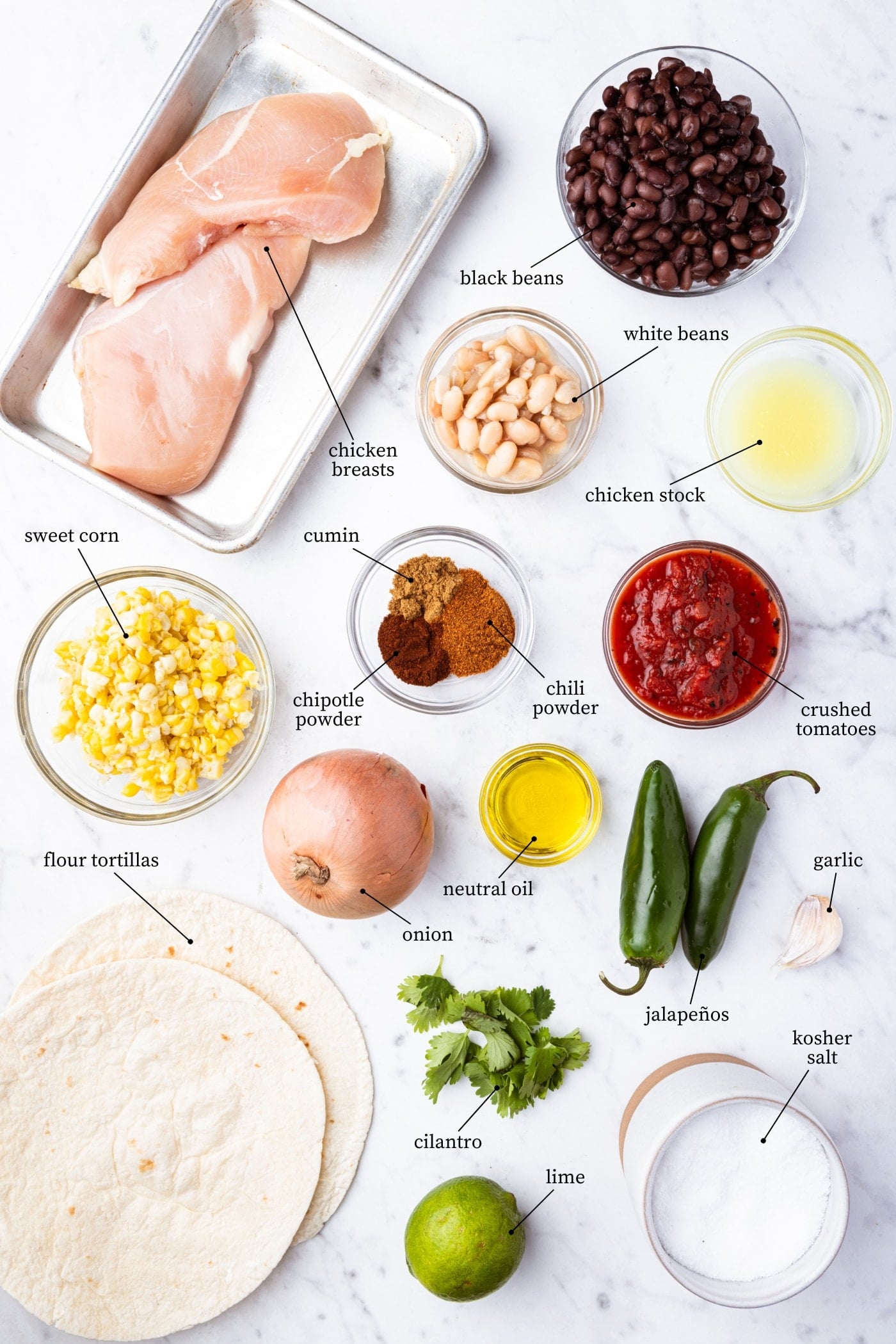 Overhead flat-lay of raw Crockpot Chicken Tortilla Soup ingredients laid out in small bowls — raw chicken breasts, black beans, corn, canned tomatoes, broth, and spices on a light marble surface