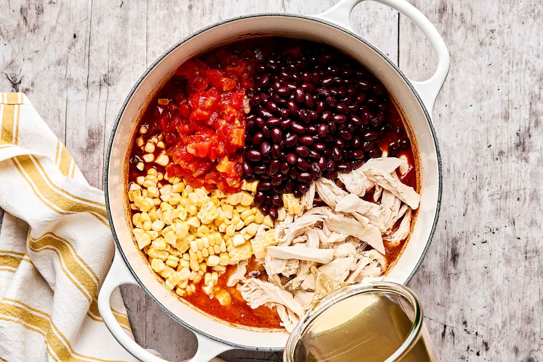 Close-up of a ladle lifting a rich scoop of Crockpot Chicken Tortilla Soup showing shredded chicken, black beans, and corn in a deep red broth, garnished with fresh cilantro and lime