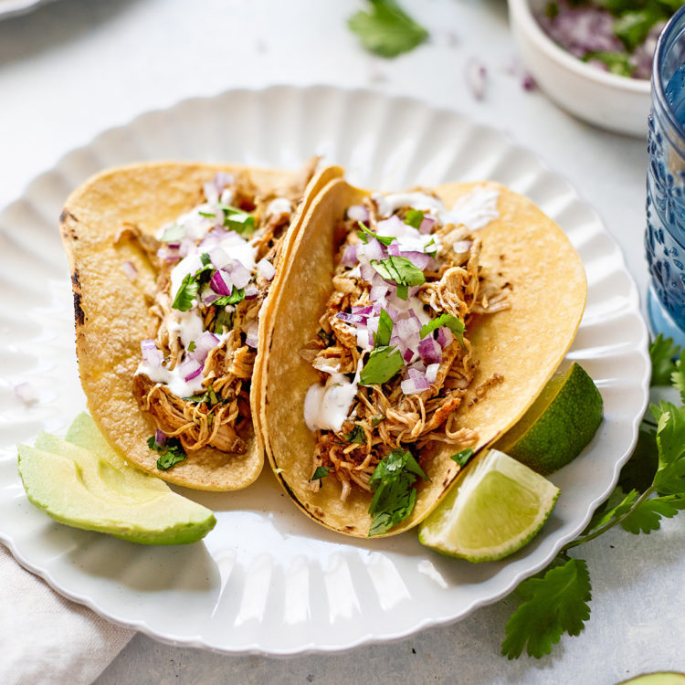 Close-up of juicy shredded Crockpot Salsa Chicken piled high in a warm flour tortilla topped with fresh cilantro, diced white onion, and a squeeze of lime