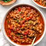 A rustic bowl of Crockpot Stuffed Pepper Soup filled with colorful bell peppers, ground beef, rice, and rich tomato broth, garnished with fresh parsley and shredded cheese on a cozy linen-covered table