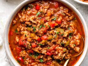 A rustic bowl of Crockpot Stuffed Pepper Soup filled with colorful bell peppers, ground beef, rice, and rich tomato broth, garnished with fresh parsley and shredded cheese on a cozy linen-covered table
