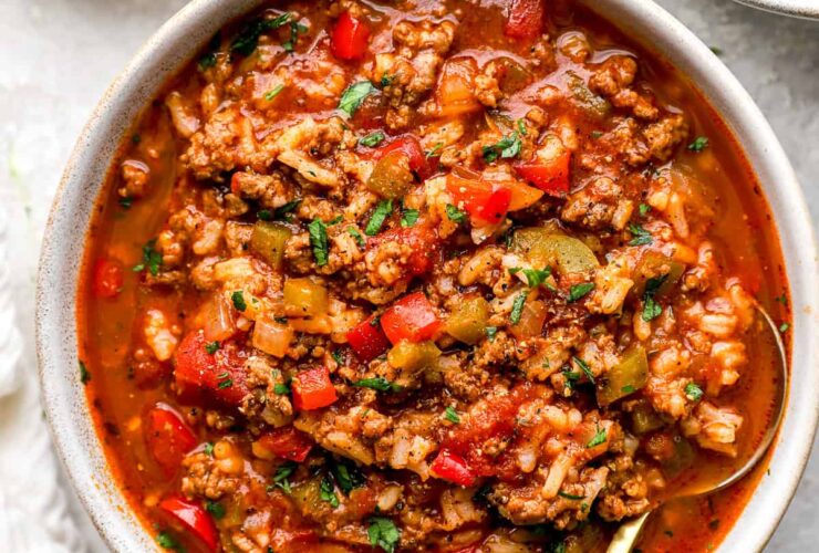 A rustic bowl of Crockpot Stuffed Pepper Soup filled with colorful bell peppers, ground beef, rice, and rich tomato broth, garnished with fresh parsley and shredded cheese on a cozy linen-covered table