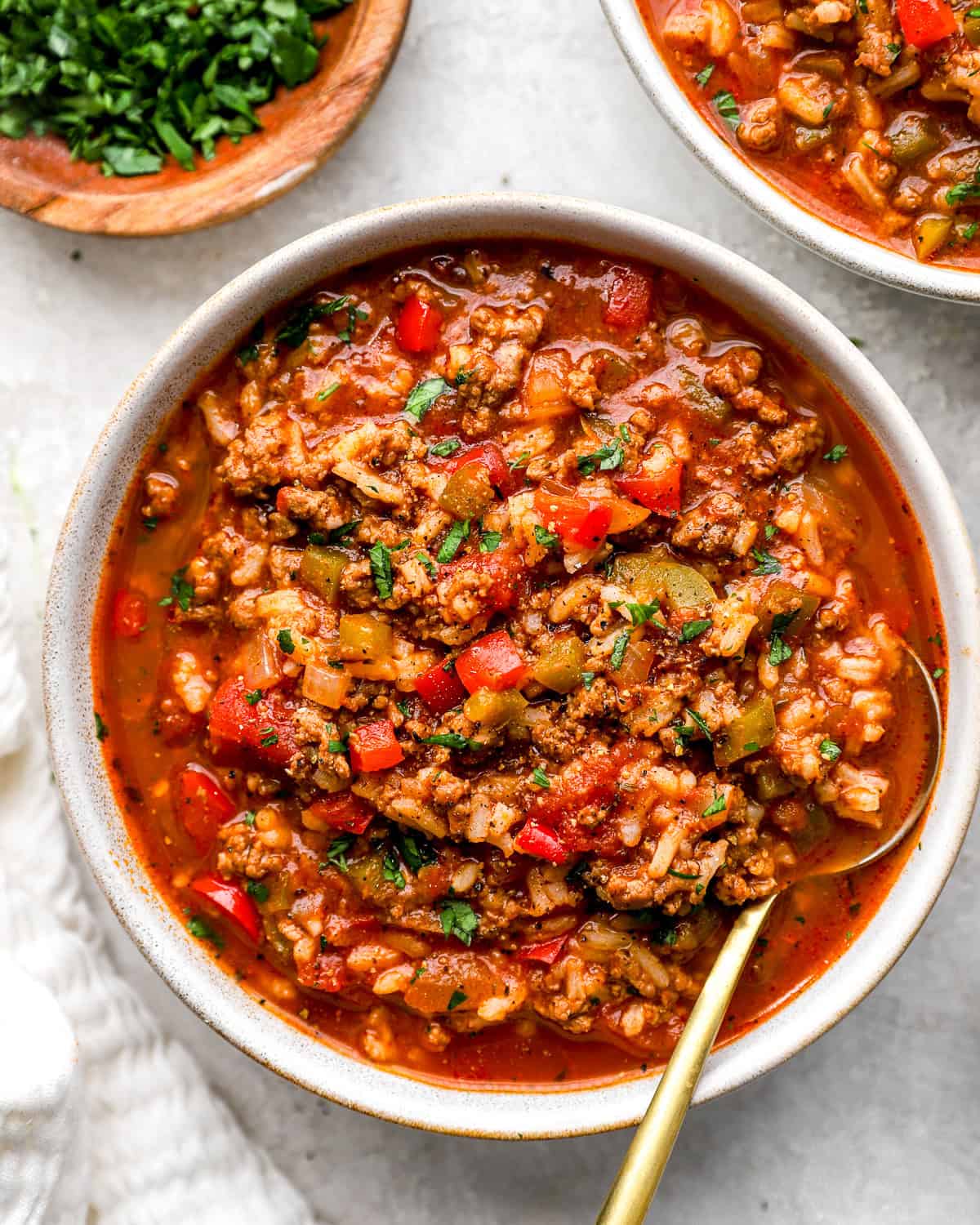 Crockpot Stuffed Pepper Soup — All the Flavor, None of the Fuss 26 A rustic bowl of Crockpot Stuffed Pepper Soup filled with colorful bell peppers, ground beef, rice, and rich tomato broth, garnished with fresh parsley and shredded cheese on a cozy linen-covered table