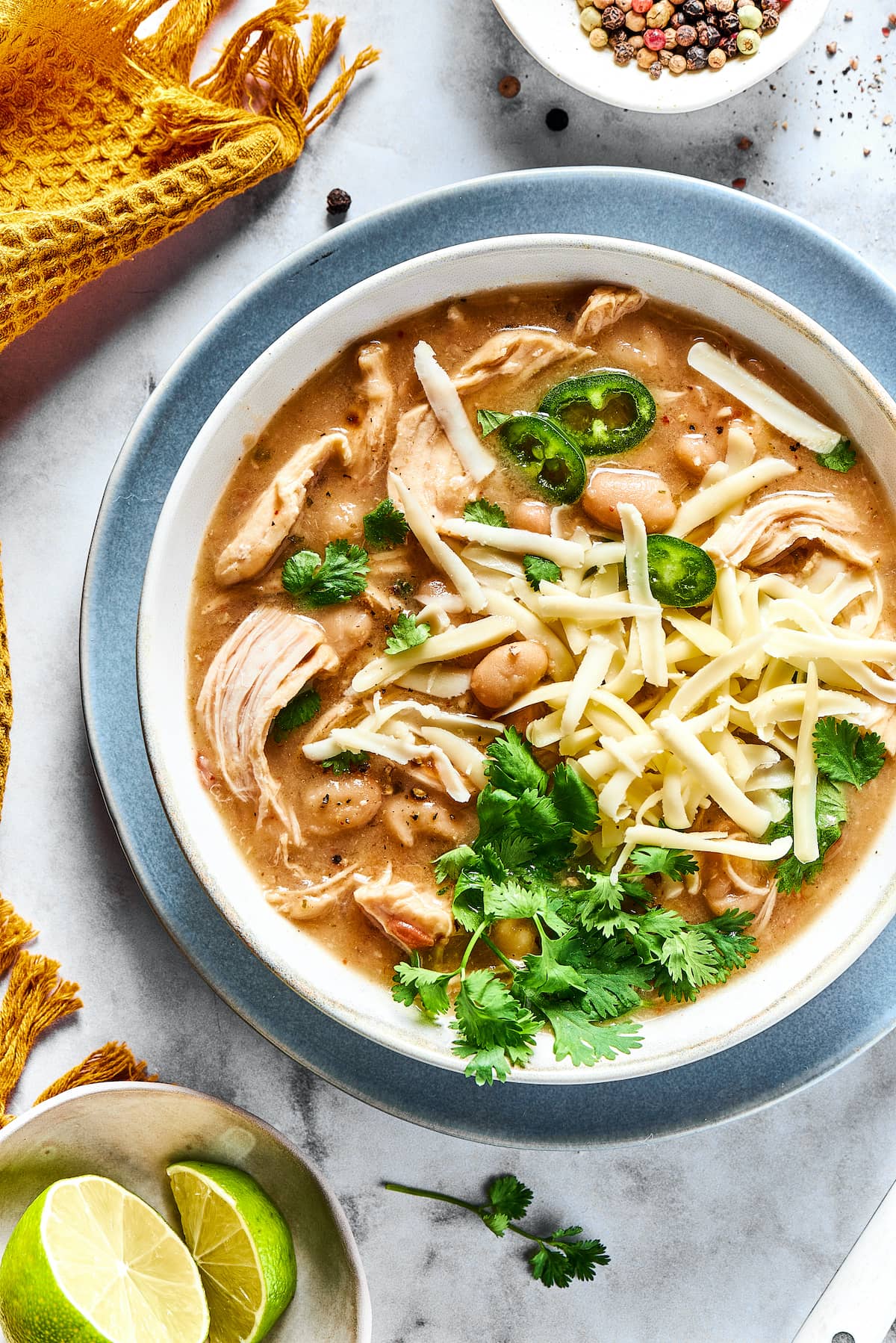 Crockpot White Chicken Chili — Creamy, Cozy, and Packed with Protein 27 An overhead flat-lay of the key Crockpot White Chicken Chili ingredients arranged on a white marble surface — raw chicken breasts, cans of white beans and green chiles, cream cheese block, chicken broth carton, and small bowls of spices including cumin and oregano