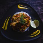 Cuban Ropa Vieja served over white rice in a wide bowl, topped with fresh cilantro and sliced olives, photographed on a rustic wooden table with warm lighting