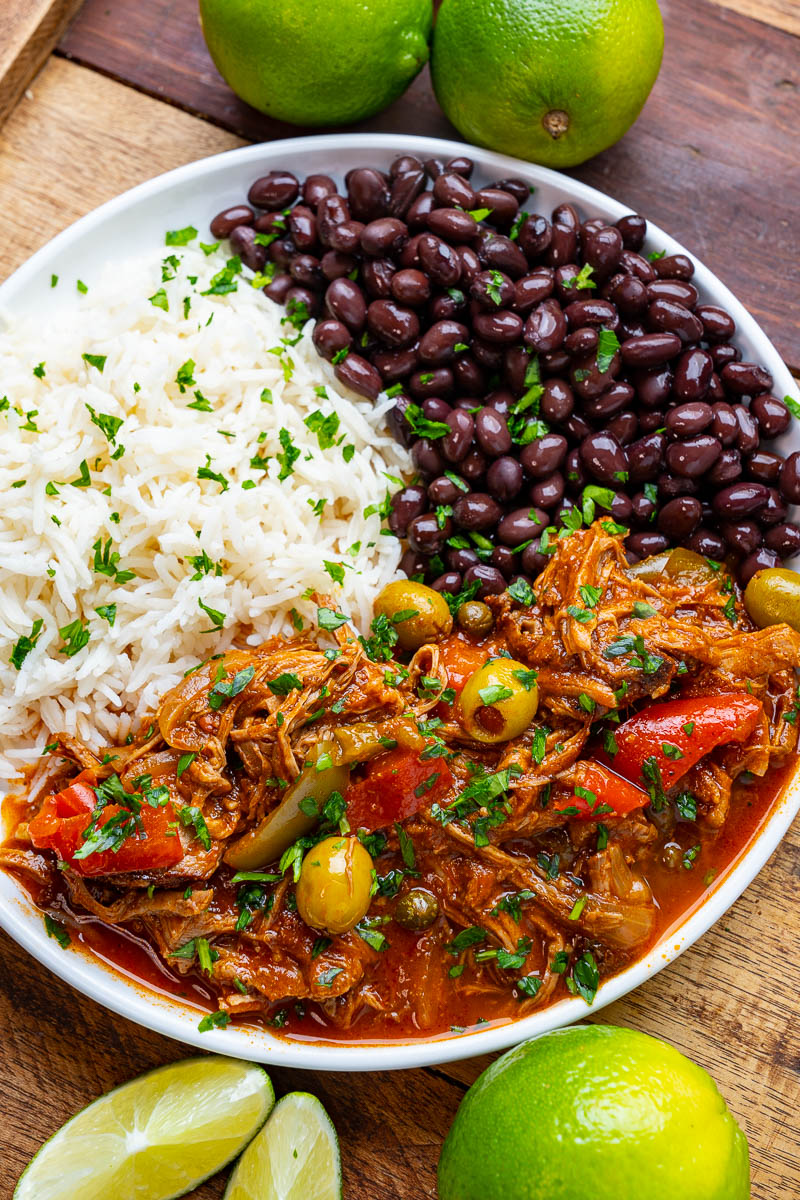 Cuban Ropa Vieja — Tender Shredded Beef in Rich Tomato Sofrito Sauce 28 Close-up of Cuban Ropa Vieja shredded beef piled over white rice, garnished with green olives, fresh cilantro, and a wedge of lime on a colorful ceramic plate