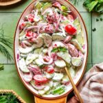 Cucumber tomato salad served in a white bowl with fresh dill and red onion, drizzled with vinegar dressing on a bright summer table