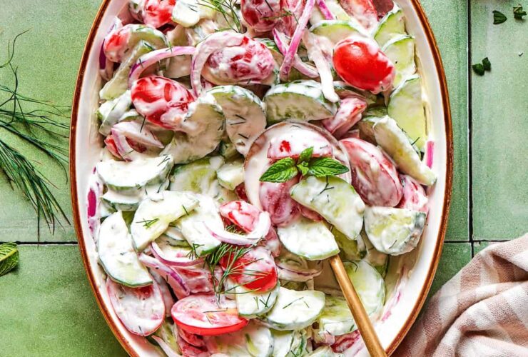 Cucumber tomato salad served in a white bowl with fresh dill and red onion, drizzled with vinegar dressing on a bright summer table