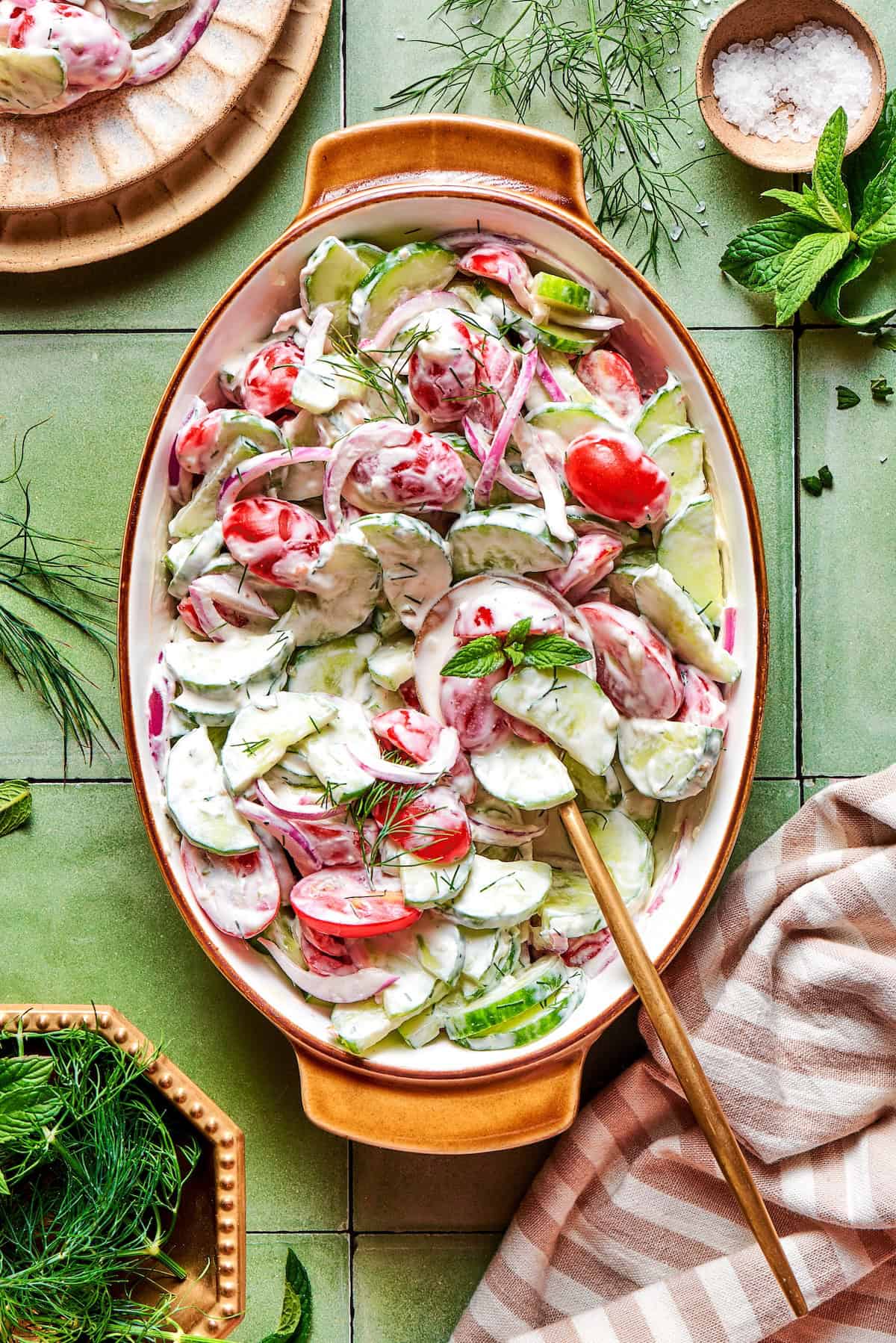 Cucumber tomato salad served in a white bowl with fresh dill and red onion, drizzled with vinegar dressing on a bright summer table
