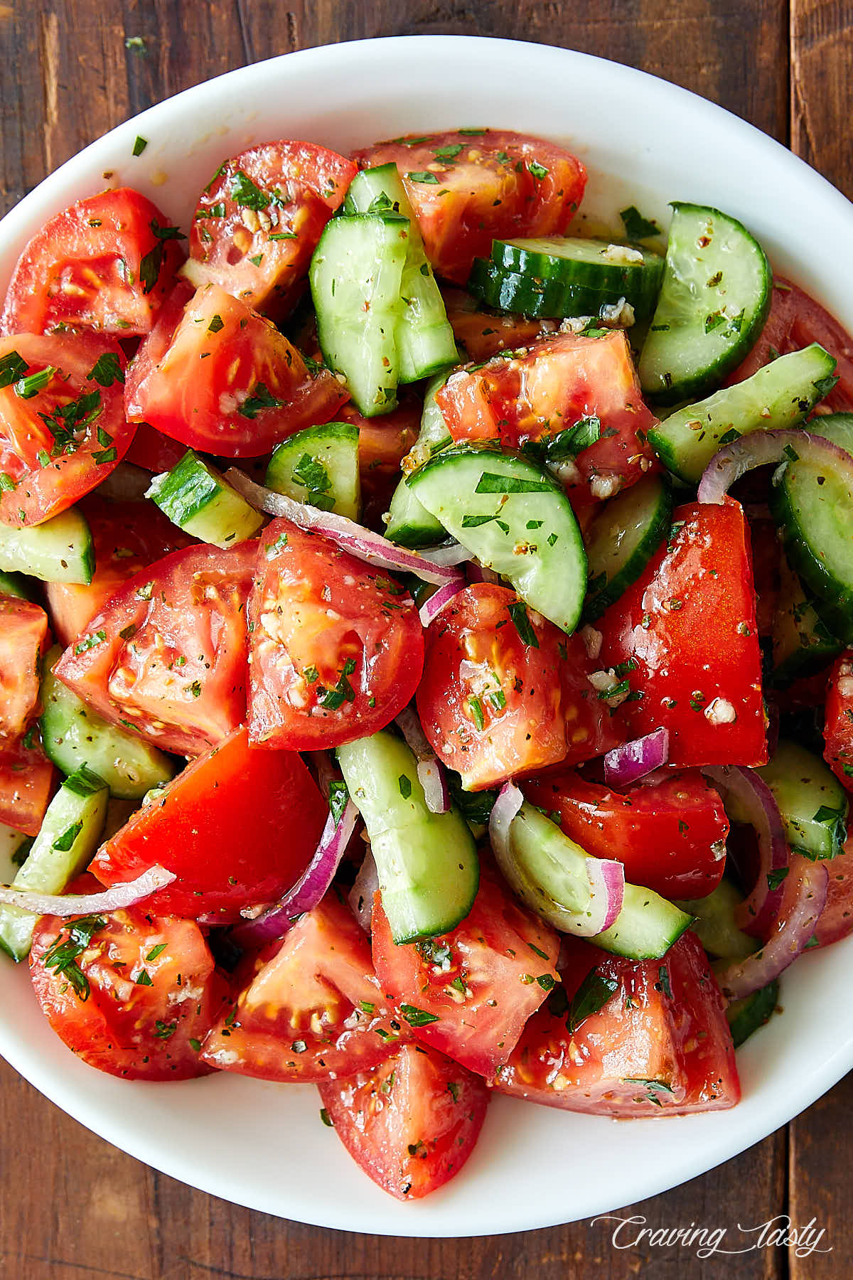 Close-up of cucumber tomato salad in a rustic bowl with visible fresh dill, red onion rings, and a glossy vinegar dressing, with a fork resting on the side