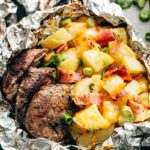 Foil Packet Steak and Potato Hash beautifully served open on a plate with juices pooling around tender steak, golden potatoes, and crispy bacon pieces, garnished with fresh herbs