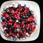 Frozen Greek yogurt berry bark broken into pieces on a white marble surface, topped with fresh strawberries, blueberries, and raspberries, drizzled with honey, bright natural lighting