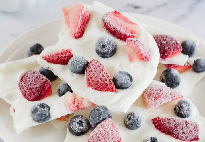 Frozen Greek yogurt berry bark broken into pieces on a white marble surface, topped with fresh strawberries, blueberries, and raspberries, drizzled with honey, bright natural lighting