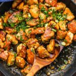 Garlic Butter Chicken Bites and Potatoes served in a cast iron skillet, garnished with fresh parsley and lemon wedges on a rustic wooden table