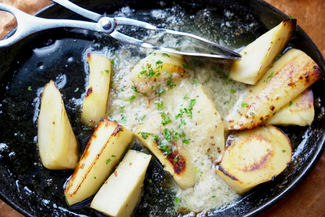 Close-up of golden garlic butter chicken bites and crispy potatoes in a skillet, with melted butter pooling around the edges and fresh parsley scattered on top