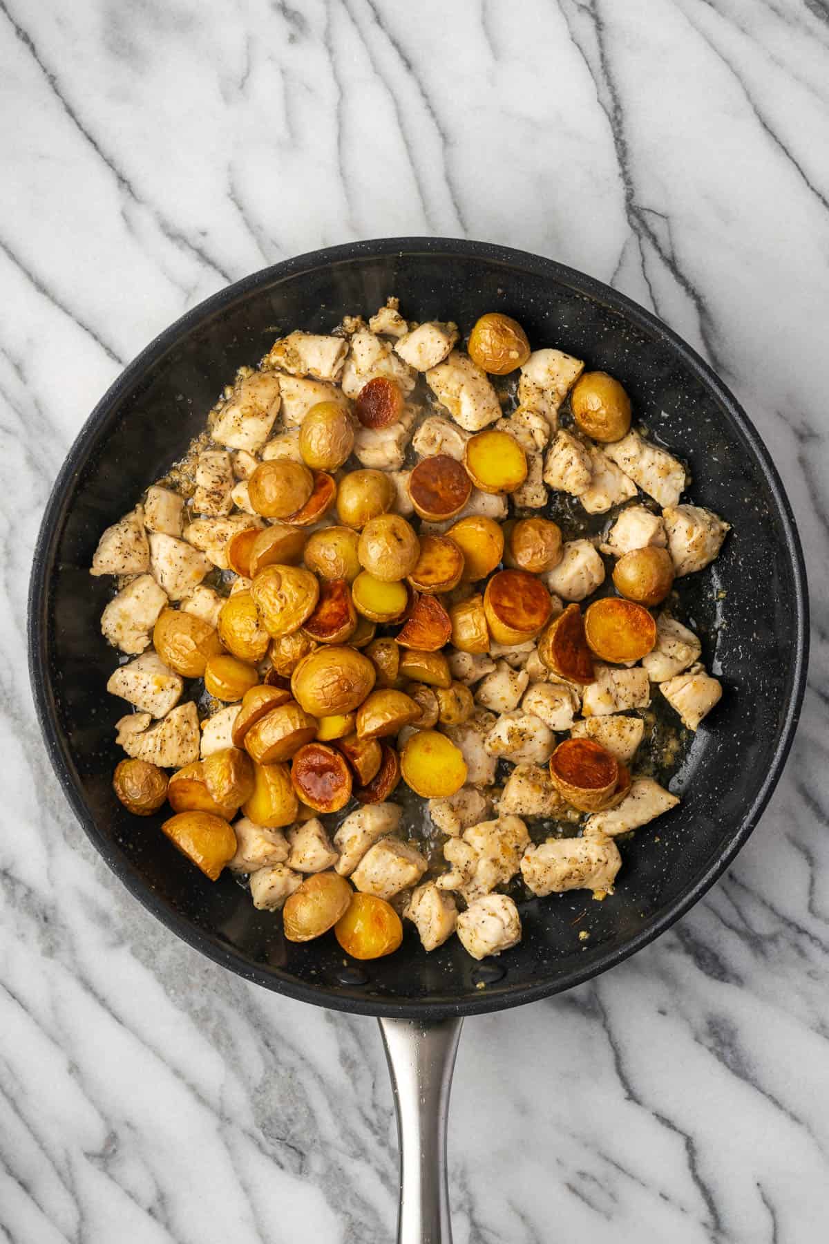 Close-up of golden garlic butter chicken bites and crispy potatoes in a skillet, with melted butter pooling around the edges and fresh parsley scattered on top