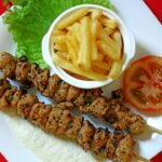 Greek Chicken Souvlaki served on a platter with warm pita, tzatziki, sliced tomatoes, red onion, and fresh parsley garnish