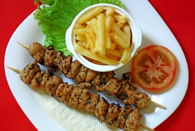 Greek Chicken Souvlaki served on a platter with warm pita, tzatziki, sliced tomatoes, red onion, and fresh parsley garnish