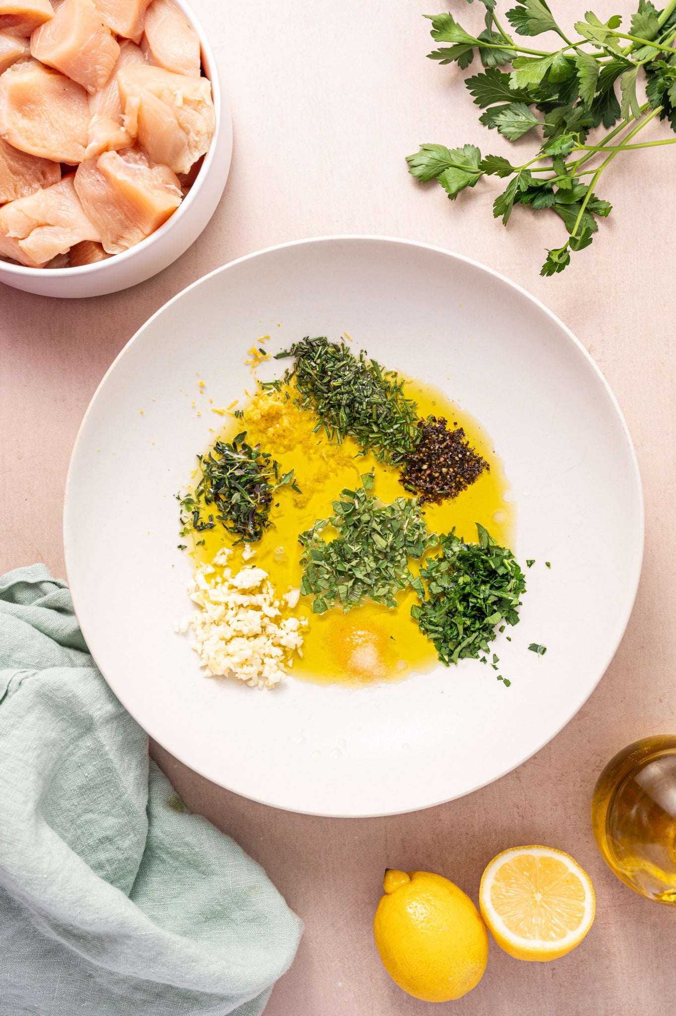 Overhead flat lay of Greek Chicken Souvlaki marinade ingredients including olive oil, lemon halves, garlic cloves, dried oregano, red wine vinegar, and raw chicken thighs on a wooden cutting board