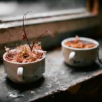 A golden-topped green bean casserole in a white ceramic baking dish, garnished with extra crispy fried onions, shot from a slight angle on a rustic wood Thanksgiving table