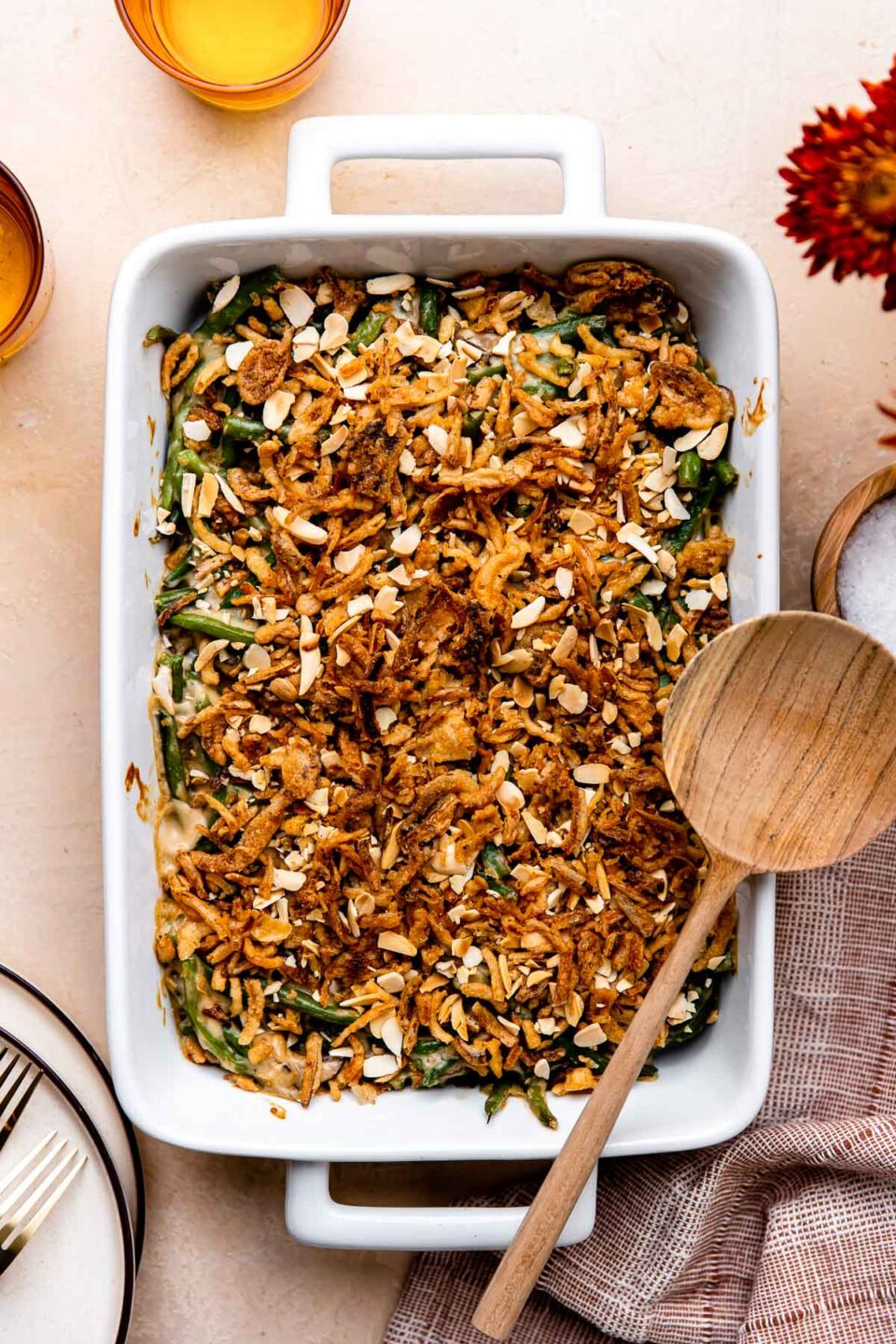 A golden-topped green bean casserole in a white ceramic baking dish, garnished with extra crispy fried onions, shot from a slight angle on a rustic wood Thanksgiving table