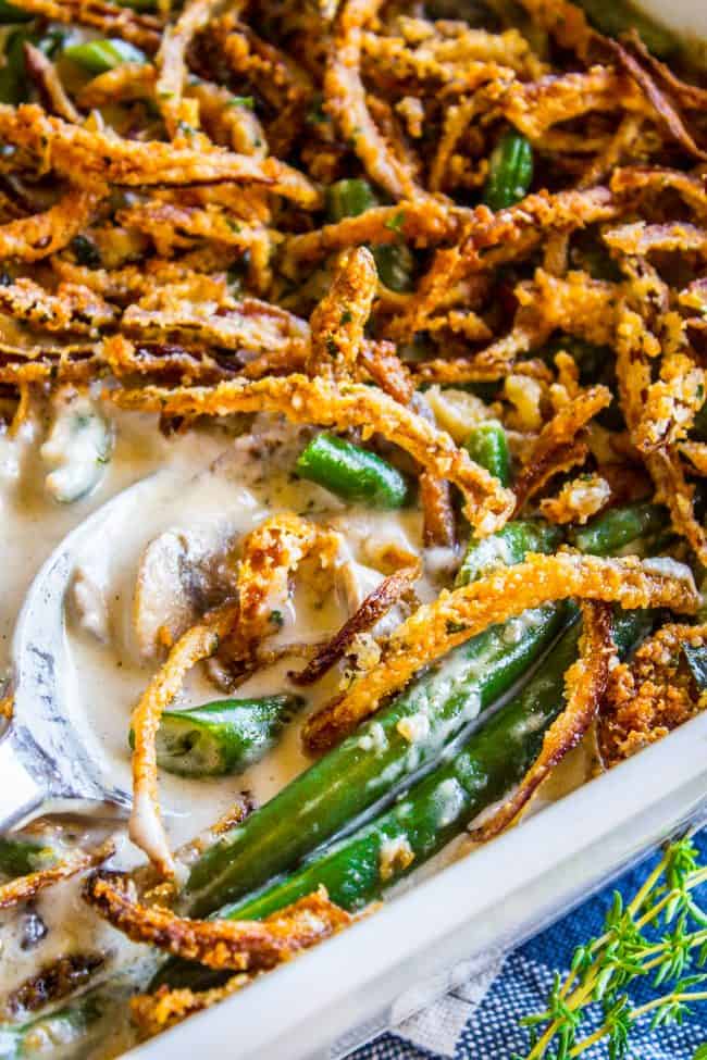 A close-up spoonful of green bean casserole being lifted from the dish, showing the creamy mushroom sauce coating the bright green beans and golden crispy onions on top
