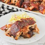 Grilled BBQ ribs fall off the bone plated on a wooden board with coleslaw and cornbread, overhead shot in natural summer light