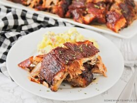 Grilled BBQ ribs fall off the bone plated on a wooden board with coleslaw and cornbread, overhead shot in natural summer light