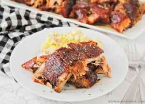 Grilled BBQ ribs fall off the bone plated on a wooden board with coleslaw and cornbread, overhead shot in natural summer light