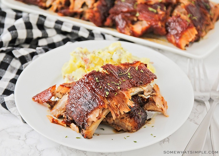 Grilled BBQ ribs fall off the bone plated on a wooden board with coleslaw and cornbread, overhead shot in natural summer light