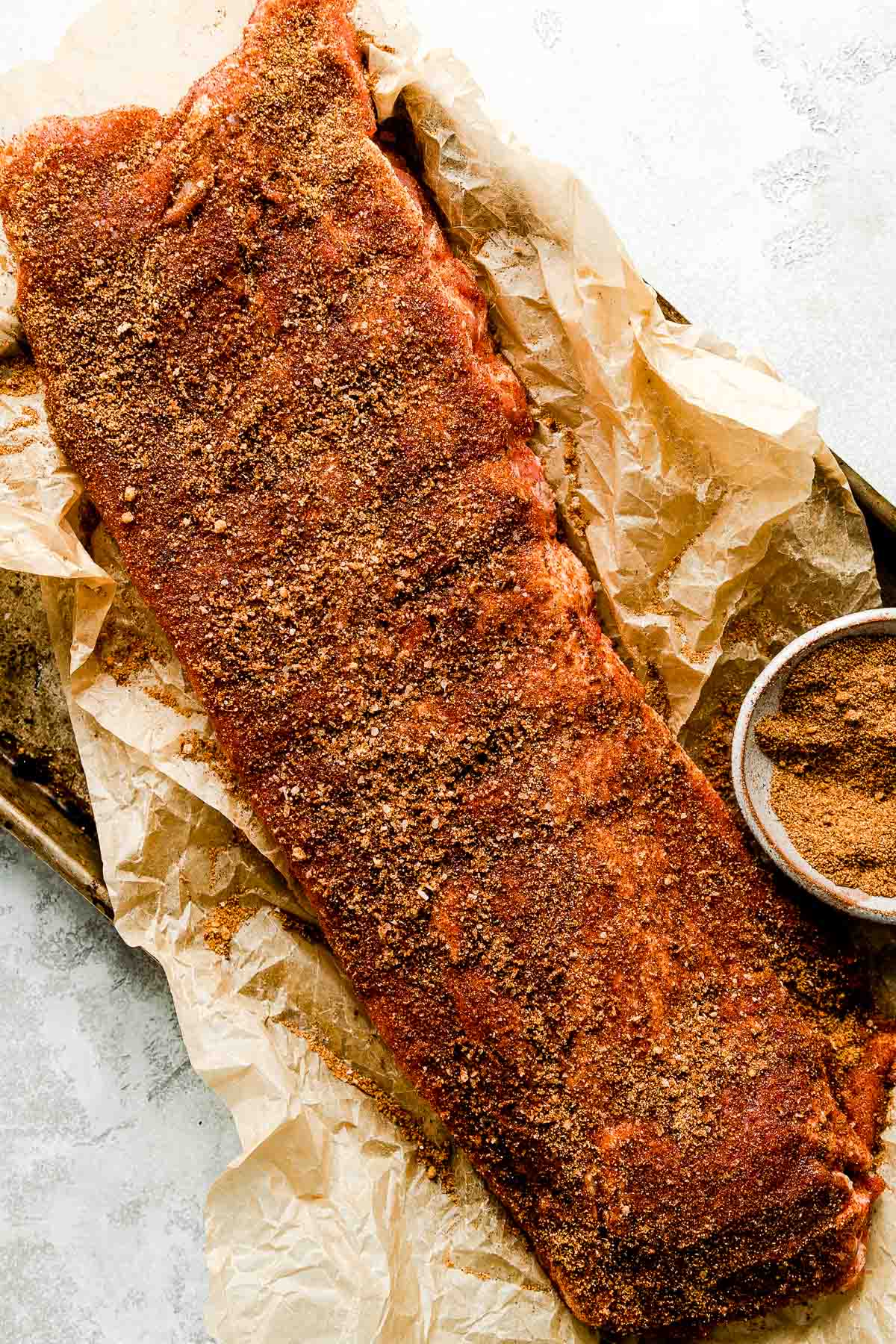 Dry rub ingredients and baby back ribs laid out on a clean marble surface, step-by-step prep shot with small bowls of spices